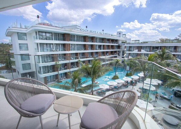 Ein Hotelbalkon mit Korbstühlen, einem Pool und Blick auf die mehreren Stockwerke und Balkone des Gebäudes.