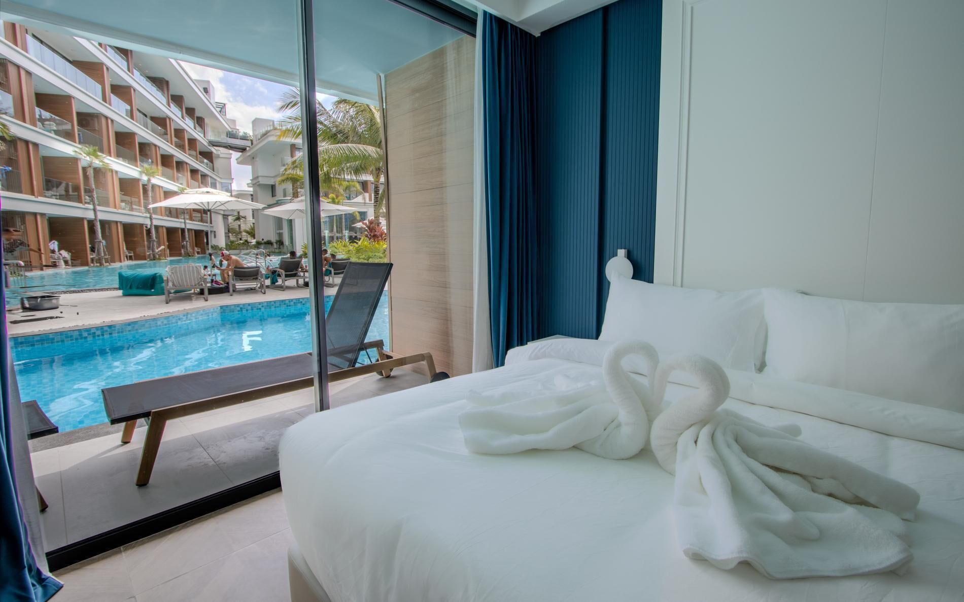 A hotel room with a bed, a view of a swimming pool, and a balcony with a view of the hotel building.