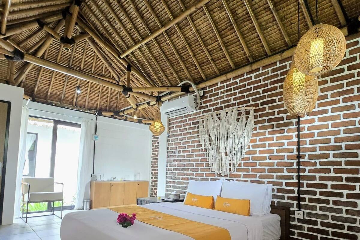 A spacious bedroom with a large bed, a brick wall, and a thatched ceiling.