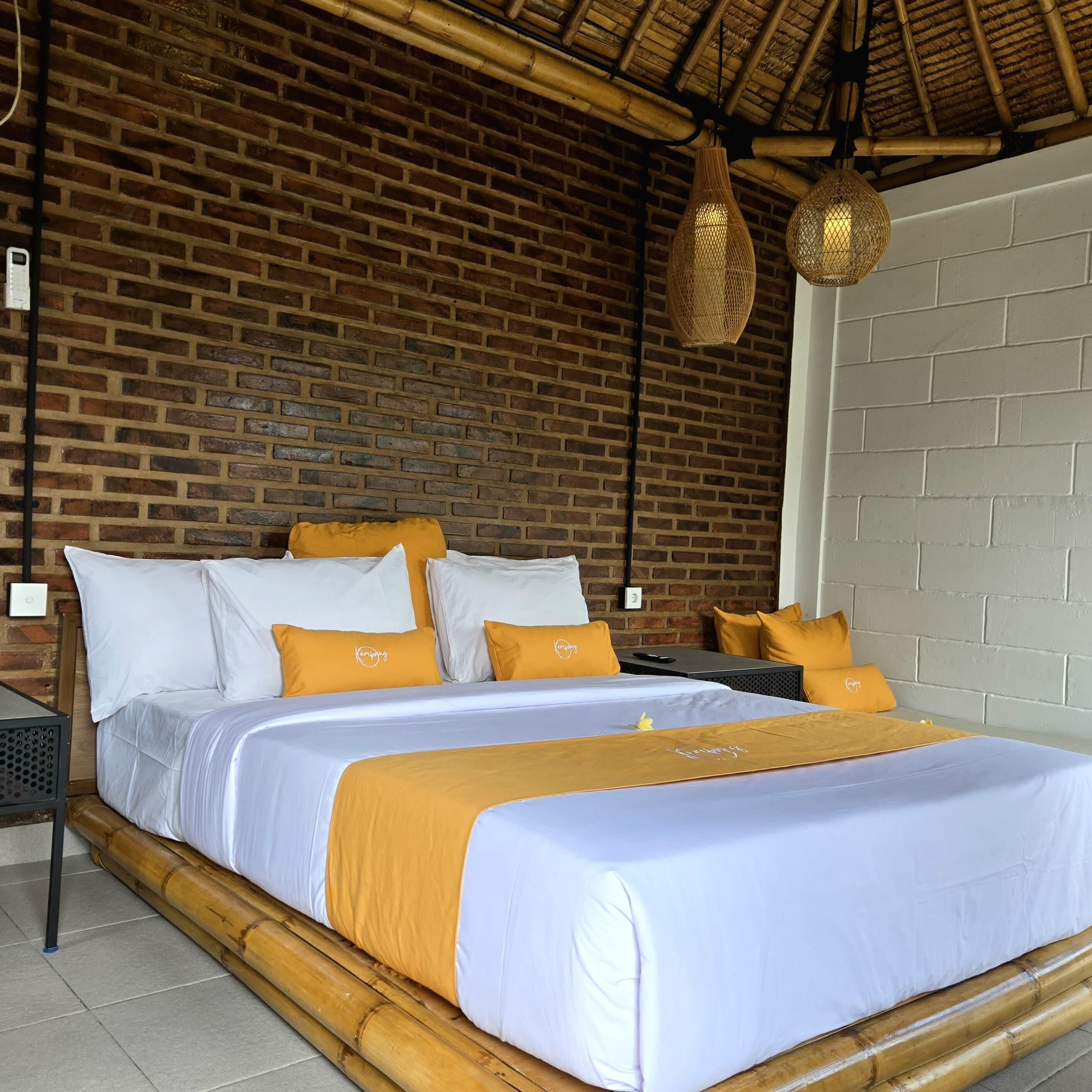 A bed with white and orange bedding, a brick wall, and a woven light fixture.