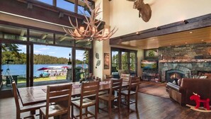 A spacious living room with a stone fireplace, wooden furniture, and large windows overlooking a scenic outdoor area. - Luxury Hope Waterfront Home and Guest House (Hope)