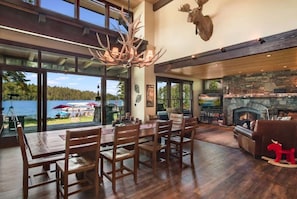 A spacious living room with a stone fireplace, wooden furniture, and large windows overlooking a scenic outdoor area.