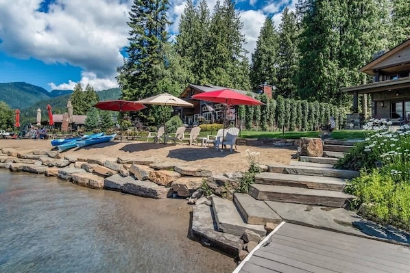 A lakeside deck with outdoor seating, a dock, and a mountain backdrop.