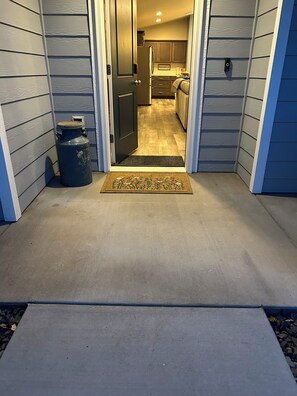 A house entrance with a concrete pathway leading to a door, a doormat, and a blue trash can. - Columbia River View near Toyota Center, large fenced yard in Kennewick (Kennewick)