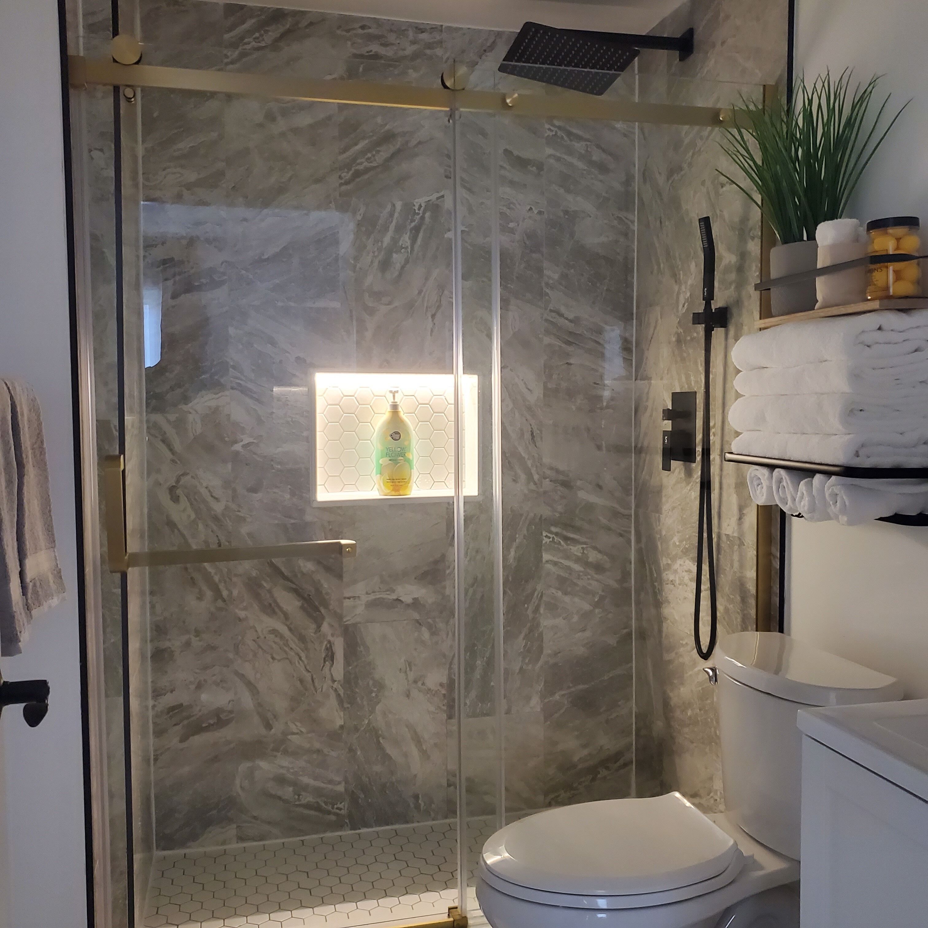 Un baño moderno con ducha de vidrio, inodoro y estante con toallas.