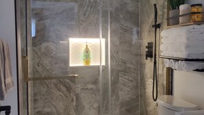 A modern bathroom with a glass-enclosed shower, a toilet, and a shelf with towels.