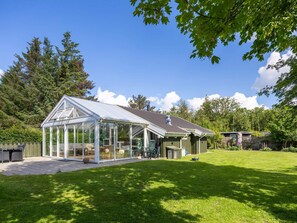 Ein Wintergarten mit Terrassenbereich, umgeben von einem gepflegten Rasen und Bäumen.