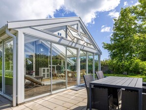 Ein Wintergarten mit Glasdach, ein Essbereich mit Korbmöbeln und Blick auf einen Garten.
