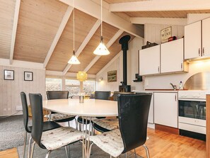 Un comedor con una mesa redonda y sillas, una cocina con armarios blancos y una estufa, y un techo de madera.