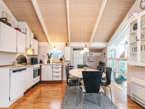 A modern kitchen with white cabinets, a dining area with a round table and chairs, and a large window providing natural light. - 4 Star Holiday Home in Hals (Hals)
