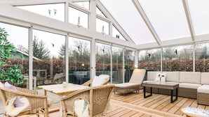 Ein Wintergarten mit Korbmöbeln, Glaswänden und einer Holzterrasse.