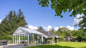 Ein Wintergarten mit Dach, eine Terrasse mit Gartenmöbeln und ein gepflegter Rasen.