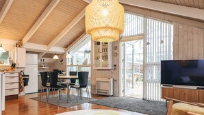 Ein modernes Interieur mit Essbereich, Küche und Wohnbereich, mit Holzböden, einem großen Fernseher und einem Esstisch mit Stühlen.