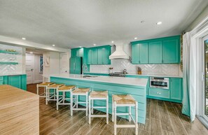 A modern kitchen with teal cabinetry, a large island with stools, and a herringbone-patterned backsplash. - Luxury House w/ Heated Pool & Spa, Walk to Beach (Siesta Key)