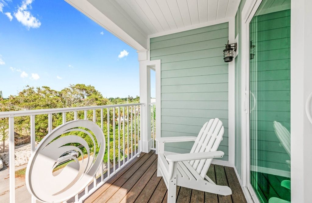 A covered porch with a white chair, a green door, and a view of the landscape.