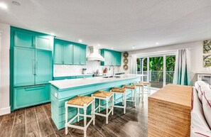 Una cocina con armarios verde azulado, una encimera blanca y una zona de bar con taburetes.