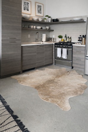 A modern kitchen with grey cabinetry, a stove, and a sink. There is a cowhide rug on the floor. - Luxury 2BR Downtown Apartment – Close to Mercedes-Benz Stadium – World Cup 2026 (Atlanta)