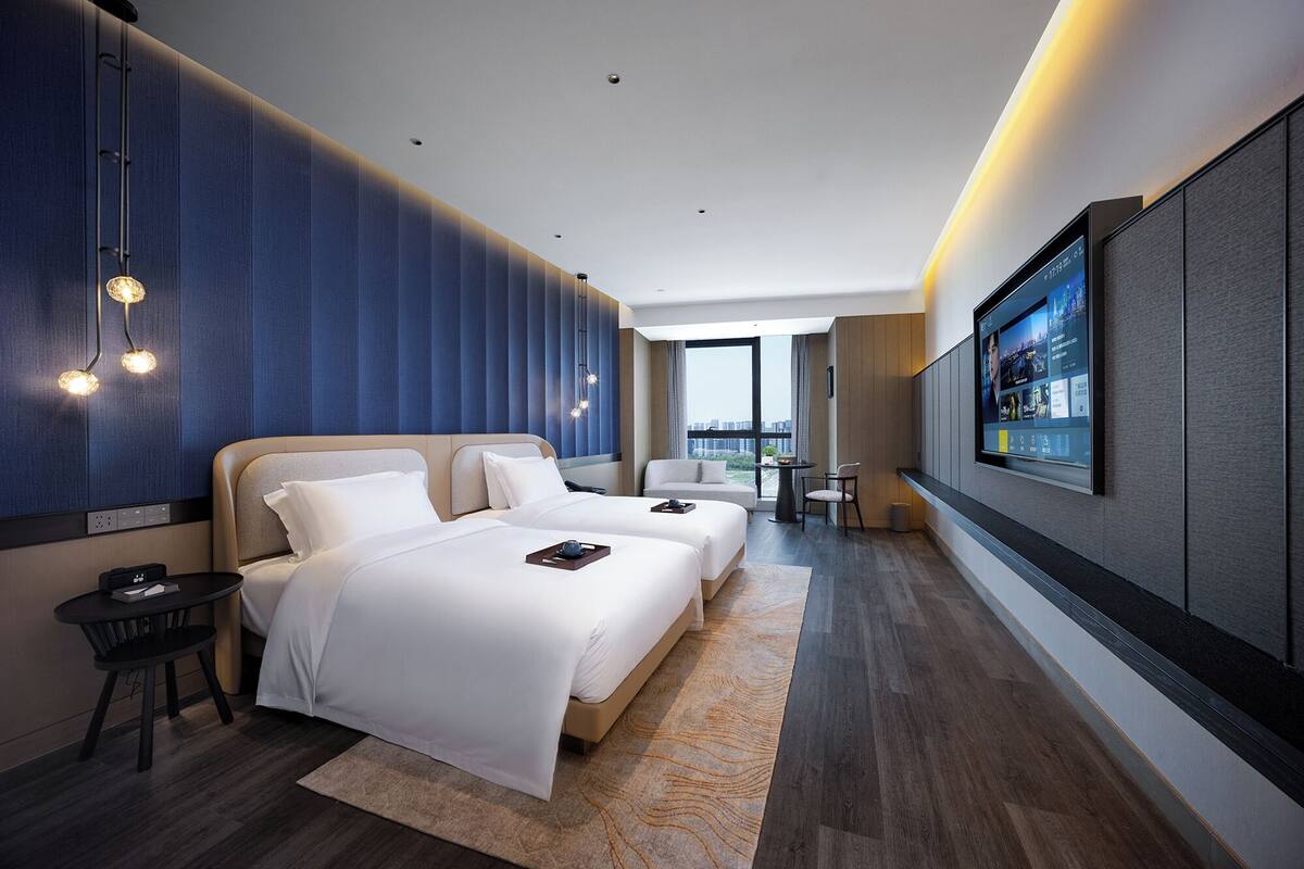 Ein modernes Hotelzimmer mit zwei Betten, einem Fernseher, einem Schreibtisch und Blick auf die Stadt.