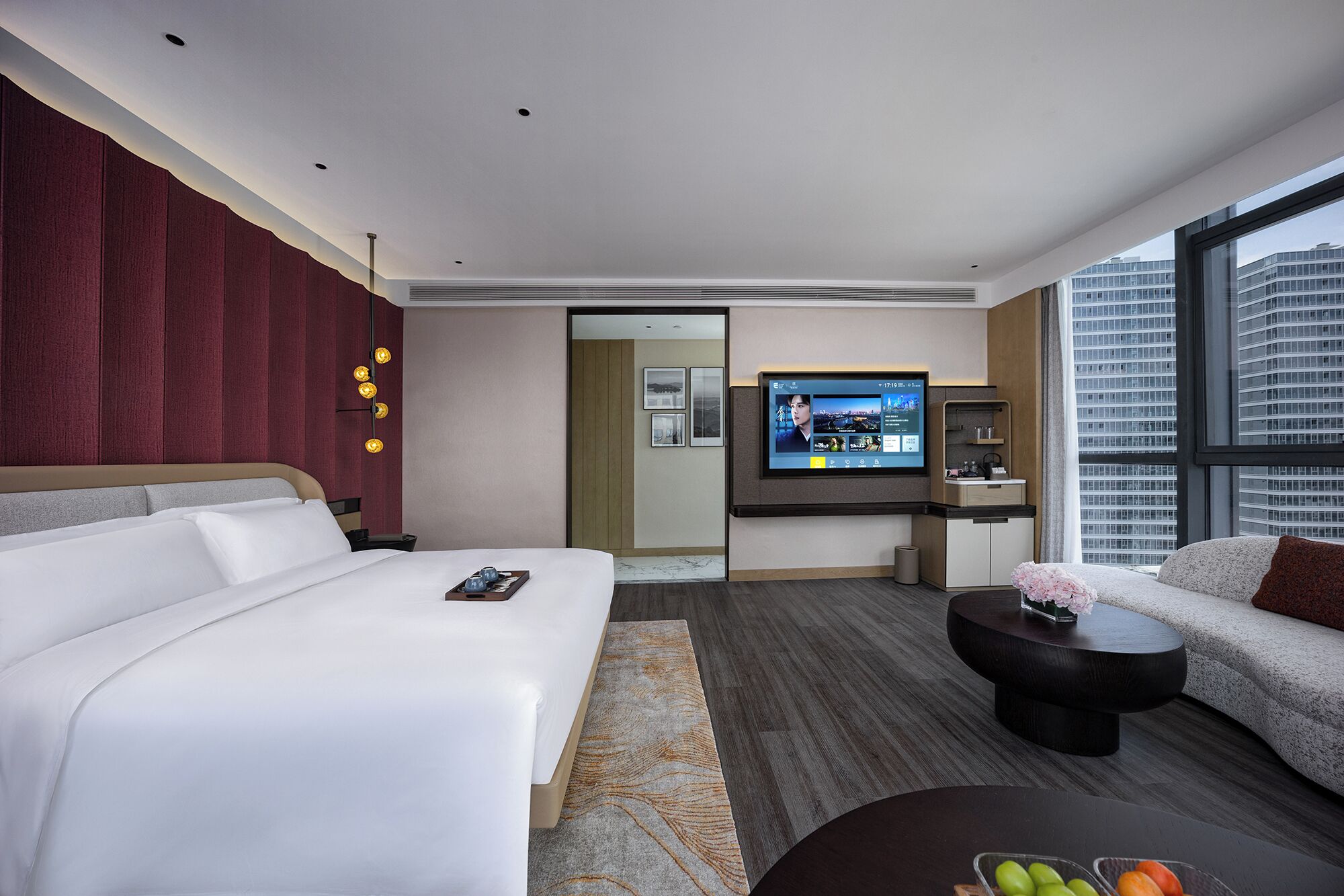 A hotel room with a bed, a TV, a sofa, a coffee table, and a view of the city.