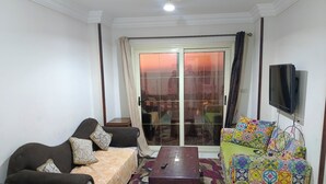 Una sala de estar con un sofá, una mesa de centro, un sillón colorido y un televisor montado en la pared.