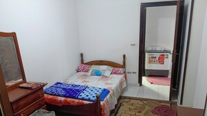 Un dormitorio con cama, cómoda, espejo, cesto de basura, alfombra rosa y una alfombra estampada.