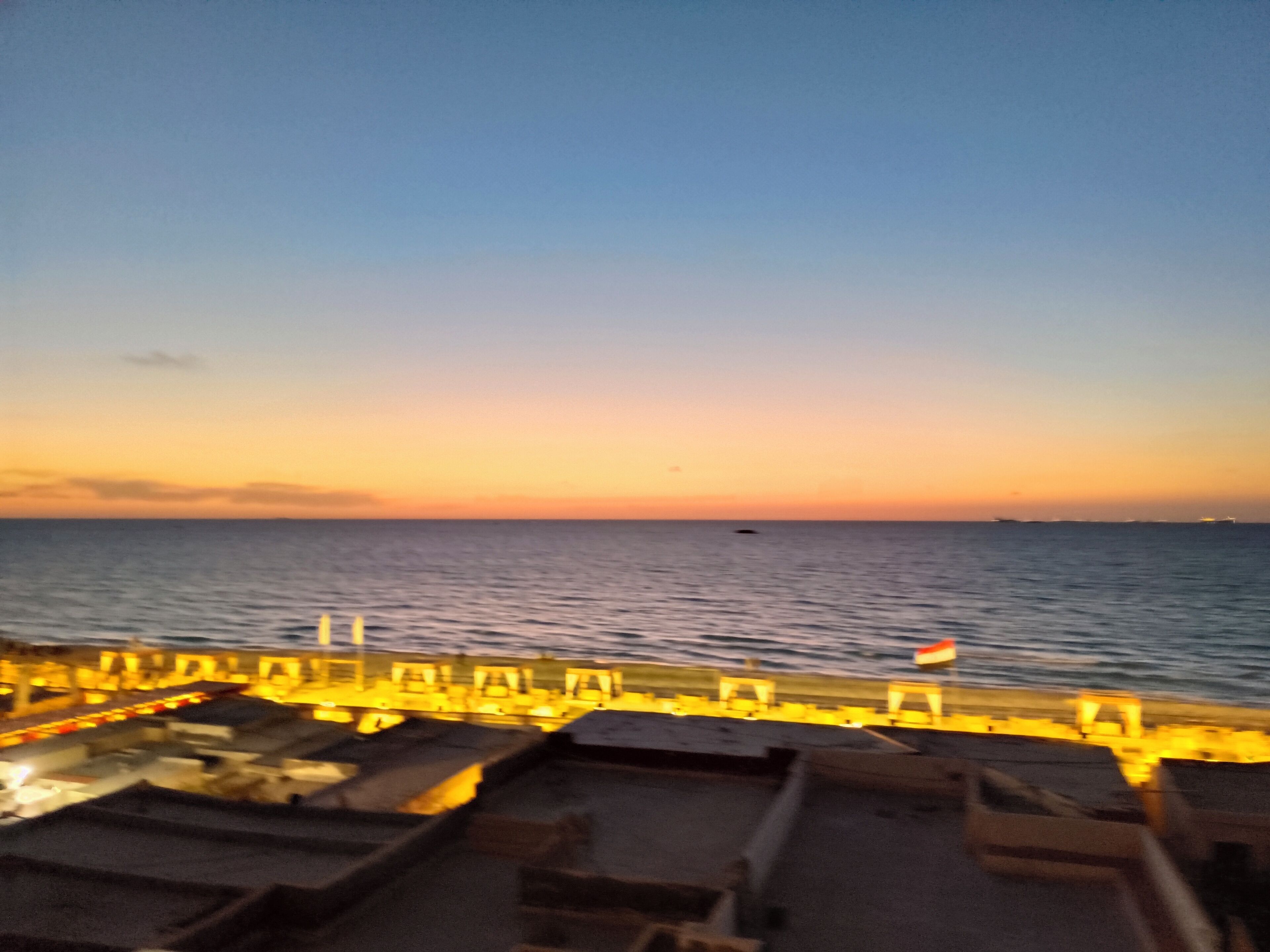 Ein Sonnenuntergang über dem Wasser von einer Pier mit Geländer und Booten.
