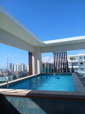 Ein Pool auf dem Dach mit Blick auf die Stadt, umgeben von modernen Gebäuden und blauem Himmel.