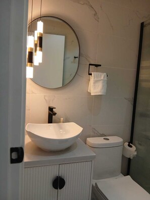 Et moderne badeværelse med et rundt spejl, en hvid vask og et toilet.