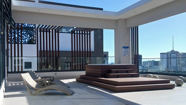 Amplia terraza en la azotea, con un diseño moderno, que cuenta con un área de descanso con sofá y sillón, y una vista despejada del horizonte de la ciudad.