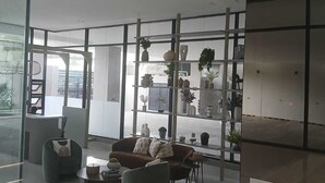 Una sala de estar moderna con un sofá, sillones y una mesa de centro. Se observan estanterías con objetos decorativos y plantas.