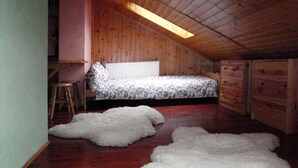 A bedroom with a sloped ceiling, wooden walls, a bed with patterned bedding, a radiator, and a white fluffy rug. - Holiday Flat in Stepnica for 7 Persons (Stepnica)