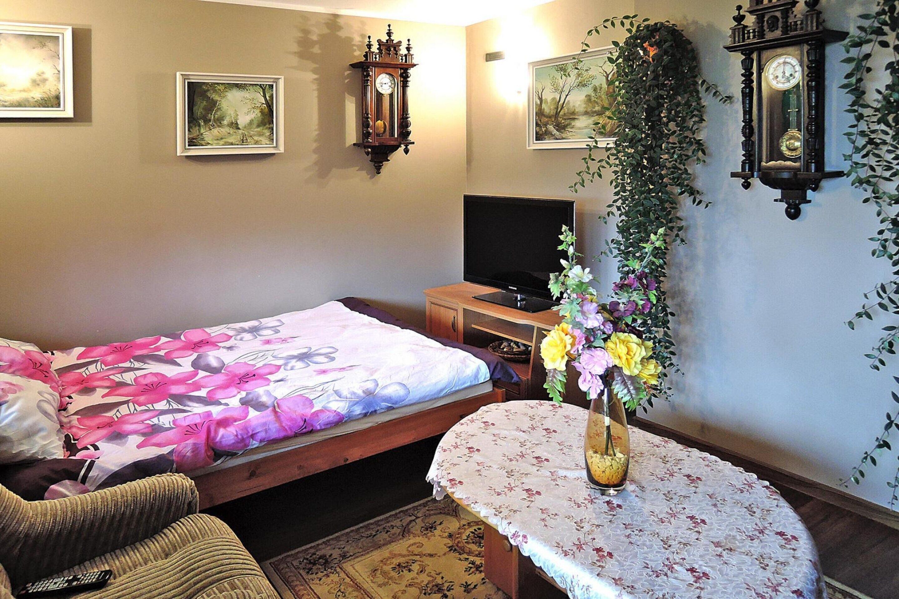 A bedroom with a bed, a TV, a clock, and a vase with flowers.