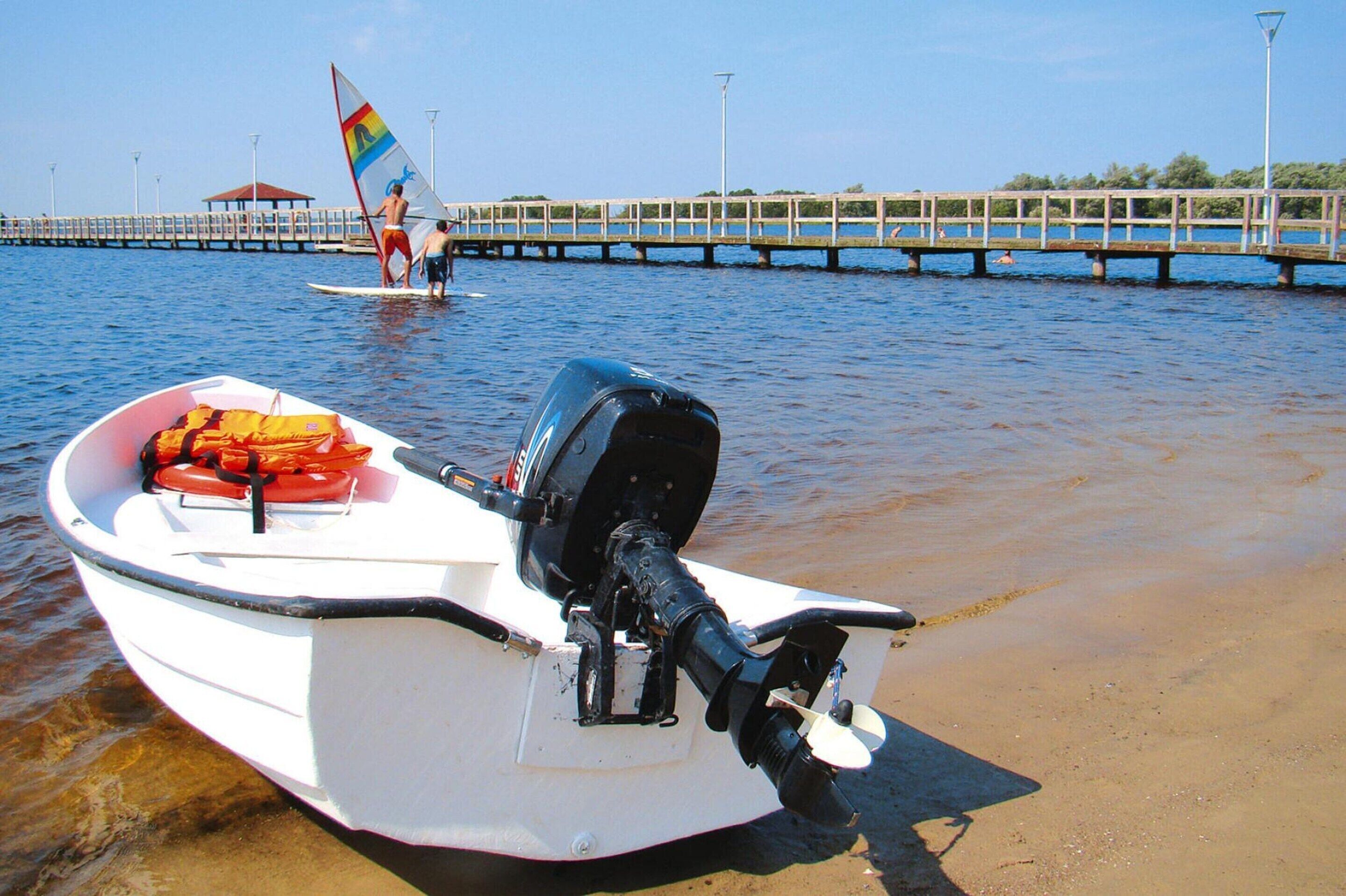 Ein kleines, weißes Boot mit Motor und Rettungsweste am Ufer.