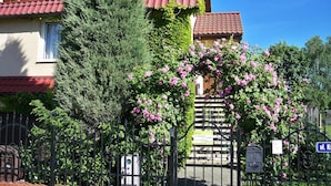 A building with a red-tiled roof, a black metal fence, and a sign with a blue background and white text. - Holiday Flat in Stepnica for 7 Persons (Stepnica)