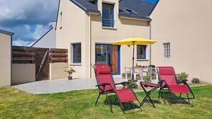 A two-story house with a patio, a yellow umbrella, and red lounge chairs. - An Ty Porzh by Interhome (Portsall/Porsguen)