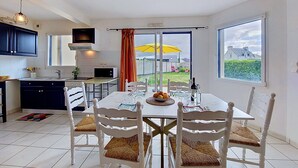 A modern kitchen with white cabinets, a dining table set for four, and a view of the garden through a sliding glass door. - An Ty Porzh by Interhome (Portsall/Porsguen)
