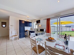 Una cocina moderna con armarios oscuros, un comedor con una mesa dispuesta para cuatro personas y un amplio ventanal con vistas al exterior.