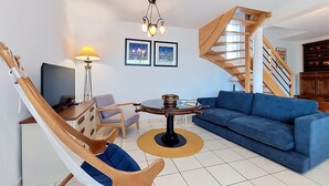 A modern living room with a blue sofa, wooden chair, round coffee table, and a staircase with wooden railings. - An Ty Porzh by Interhome (Portsall/Porsguen)