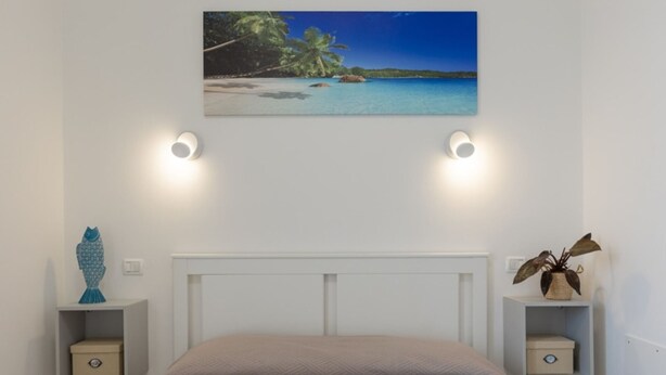 Een slaapkamer met een bed, een schilderij van een strand en twee nachtkastjes met lampen.