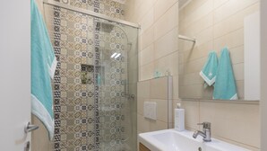 Een badkamer met douche, toilet, wastafel en spiegel.