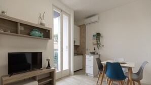 Een moderne woonkamer met een flatscreen televisie, een houten tv-meubel en een eethoek met een witte tafel en blauwe stoelen.