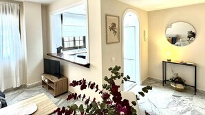 Ein modernes Wohnzimmer mit Fernseher, einem Essbereich und einer durchgehenden Tür erkennbaren Küche.