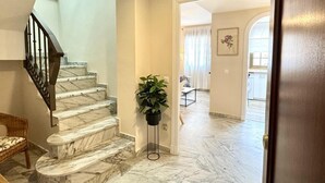 Eine Marmortreppe führt zu einer zweiten Etage, eine Topfpflanze und ein Blick in einen Essbereich mit Tisch und Stühlen.