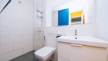 Une salle de bain moderne avec une douche à parois de verre, des toilettes blanches et un lavabo surmonté d’un miroir.