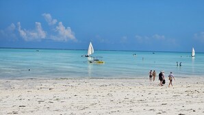A beach with clear turquoise water, a few sailboats, and people walking on the sand. - Tropical Private Garden Oasis • Soul Paje • Lagoon Pool • Walk to Beach (Paje)