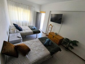 A room with two beds, a TV, a wooden dresser, a plant, and a window with curtains. - T2 with sheets, towels and barbecue. 3rd floor without elevator (Altura)