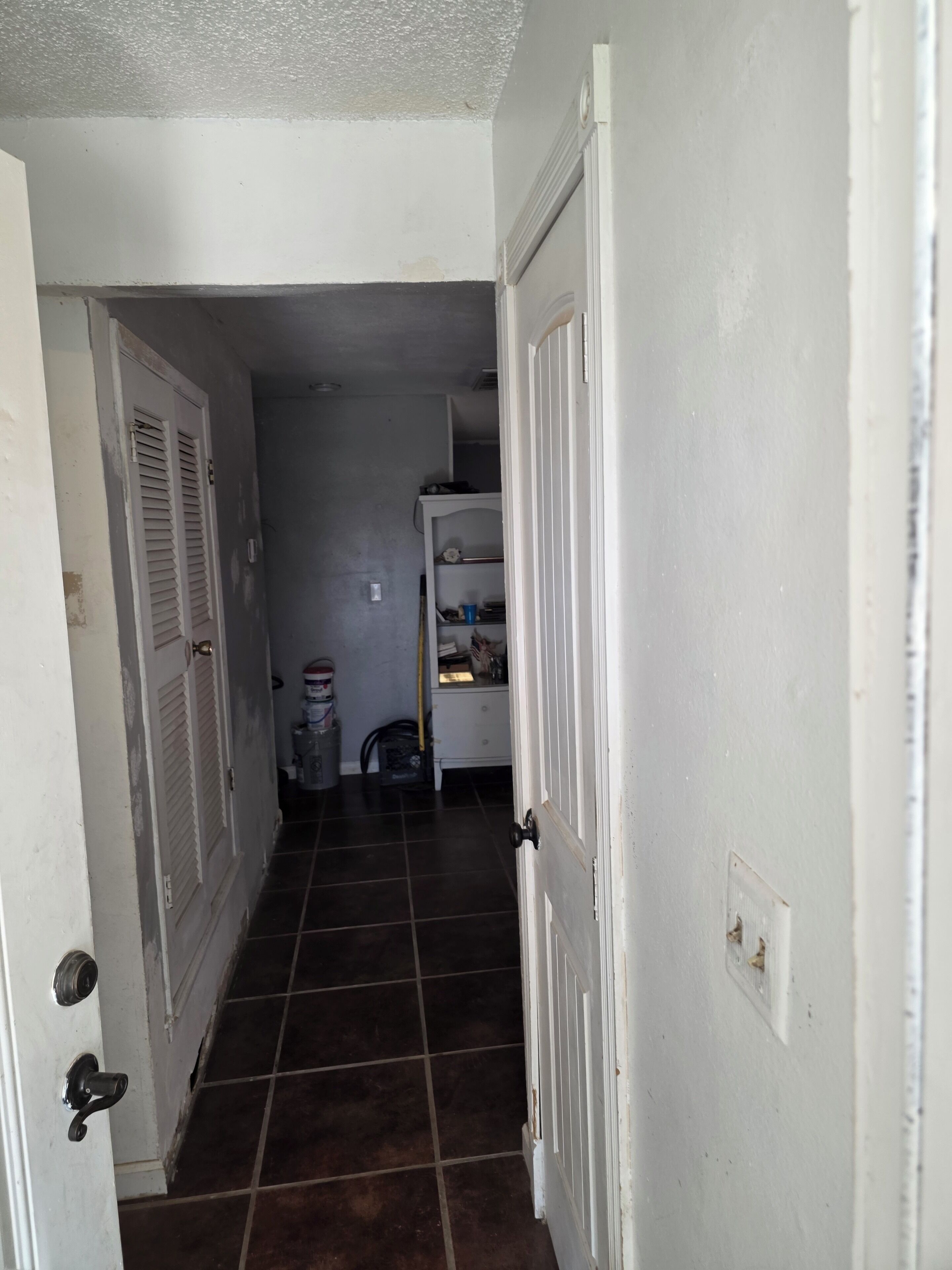 A narrow hallway with a tiled floor, white walls, and a closed door on the left.
