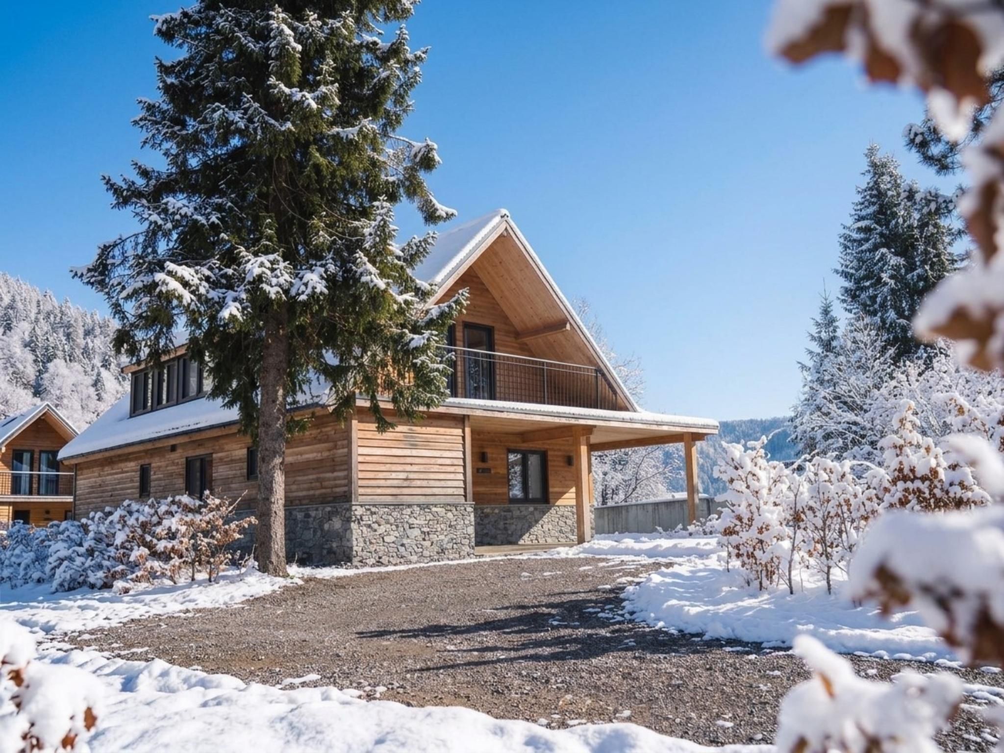 A wooden cabin with a balcony, surrounded by snow-covered trees and a clear sky.