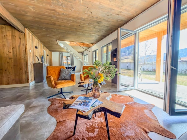Une pièce spacieuse avec un plafond en bois, une grande porte vitrée donnant sur l’extérieur, un canapé en cuir et une table avec un magazine.