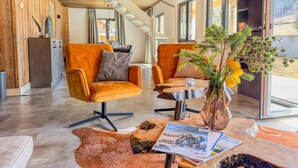 Un intérieur moderne avec un plafond en bois, deux fauteuils orange, une table basse en bois et un vase rempli de fleurs.